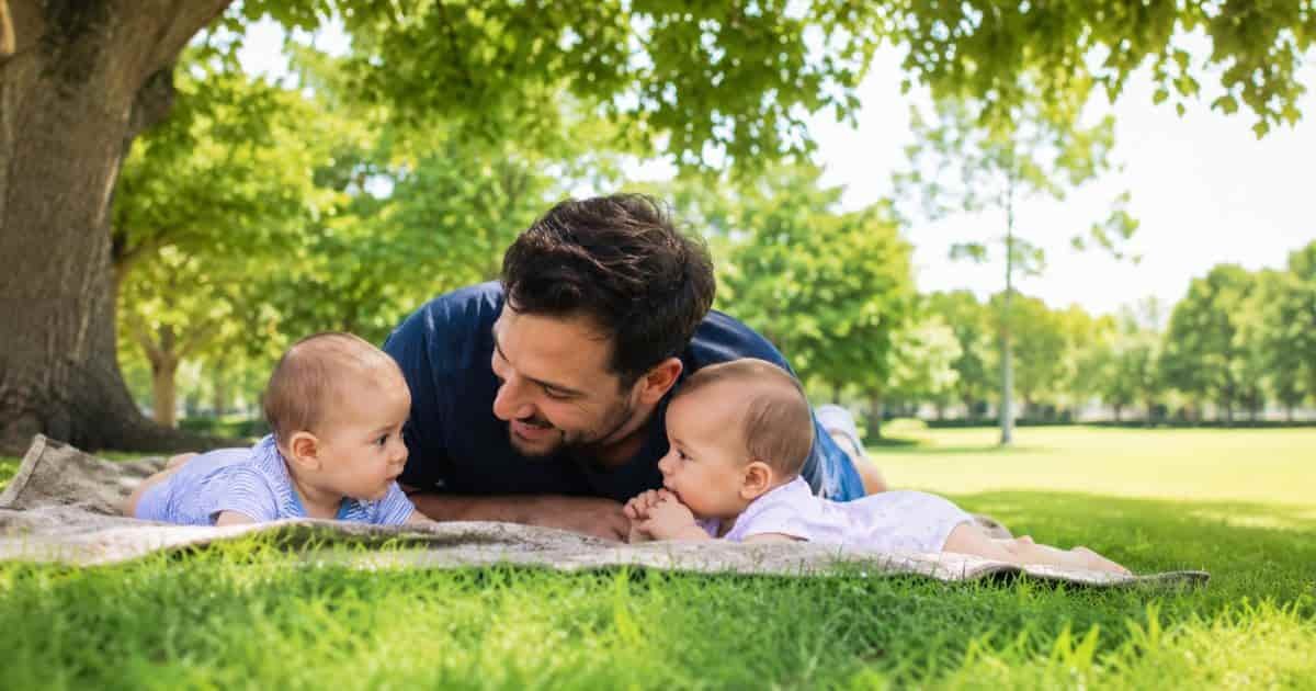 Babies are laying with his father on green area inside the park