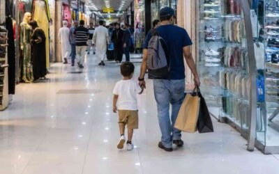 Man walking with two children carrying shopping bags through a bright indoor mall corridor lined with retail stores in Man walking with two children carrying shopping bags through a bright indoor mall corridor lined with retail stores.