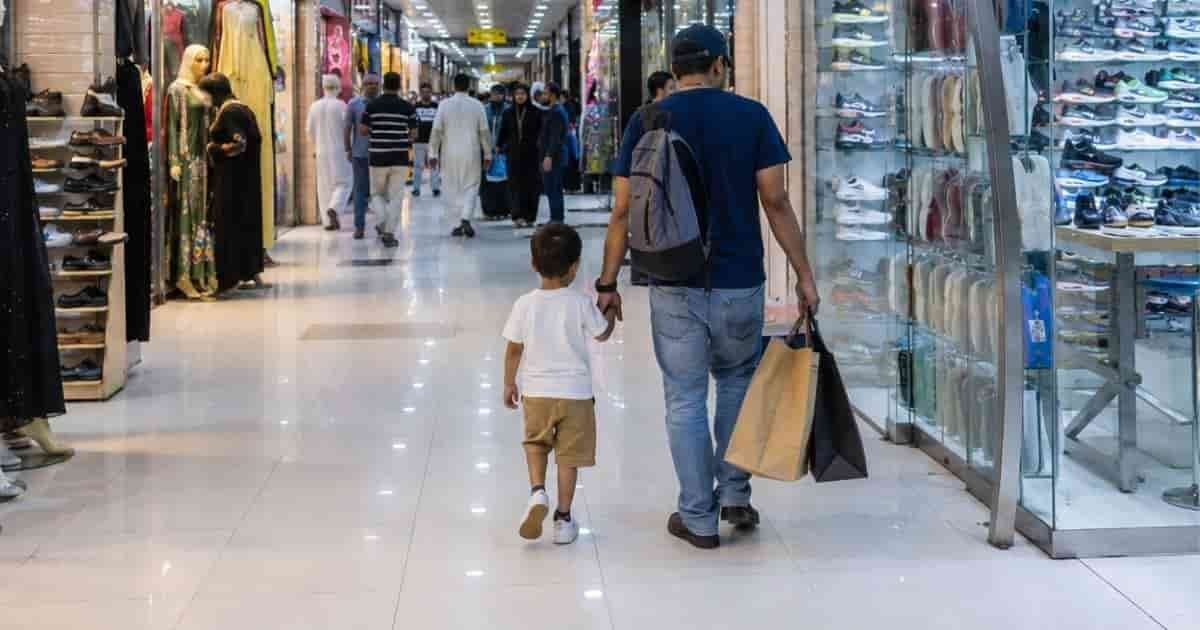 Man walking with two children carrying shopping bags through a bright indoor mall corridor lined with retail stores in Man walking with two children carrying shopping bags through a bright indoor mall corridor lined with retail stores.
