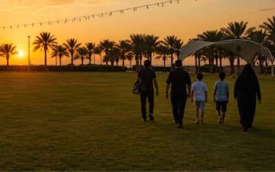 Golden hour park lawn with silhouetted family walking toward palm trees and hanging lights at sunset in Town Square Park Dubai