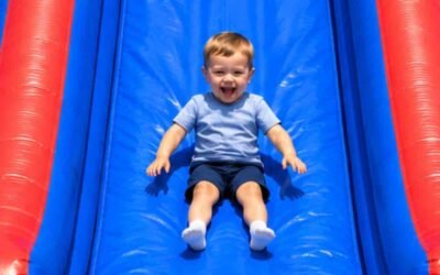 There are colorful inflatable slides side by side, with a child sliding down the center slide in an outdoor park